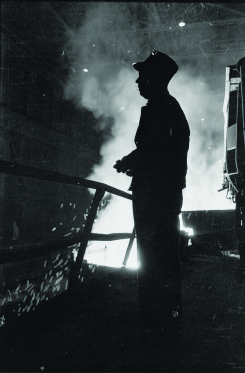 Steel worker with smelter in background.
